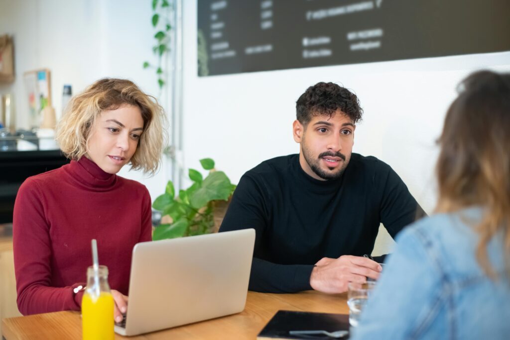 Three people working at a desk with their computers.